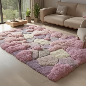 Puede incluir: Una alfombra rectangular grande con un diseño texturizado único. La alfombra presenta un patrón de secciones elevadas de forma irregular en tonos de rosa, lavanda y crema. La alfombra está colocada sobre un suelo de madera clara, con un sofá y una silla en el fondo.