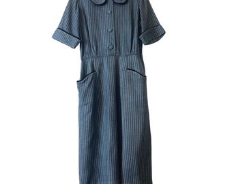 May include: A blue and white striped dress with a white collar and black trim. The dress has short sleeves and two pockets.