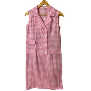 Op de afbeelding: Een roze en witte gingham jurk zonder mouwen met een dubbele rij knopen en twee zakken.