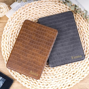 May include: Two rectangular, textured cases, one brown and one grey, with personalised names in gold lettering. The brown case reads "Anna" and the grey case reads "Emma". The cases are displayed on a woven, circular mat.