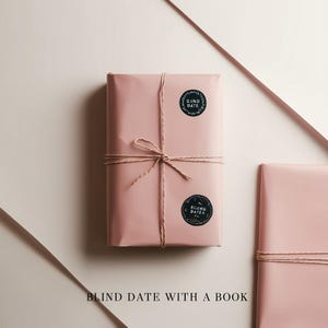 May include: A wrapped gift in pink paper, tied with twine, and adorned with two black circular stickers that read "Blind Dates." The text "Blind Date With a Book" is at the bottom of the image. The background is a light pink and white.