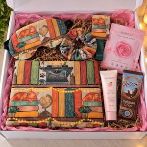 May include: A gift box containing a sleep mask, a scrunchie, and a rectangular pouch, all featuring a print of orange cats, books, and globes. Also included are a Seomou rose plant mask, a tube of peach hand cream, and a Belgian chocolate bar.