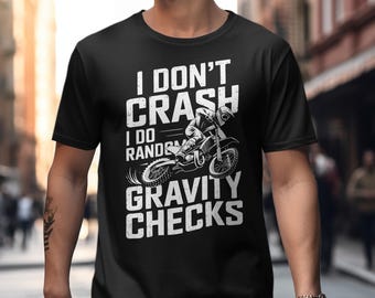 May include: Black t-shirt with a white graphic of a motocross rider and the text "I DON'T CRASH I DO RANDOM GRAVITY CHECKS". The design features a motorcycle and rider in motion.