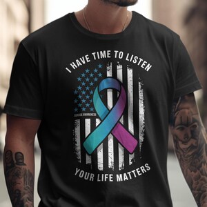 May include: Black crew neck t-shirt with a distressed American flag design. The flag features a teal and purple ribbon, with the text "I HAVE TIME TO LISTEN YOUR LIFE MATTERS" and "SUICIDE AWARENESS".