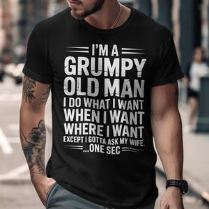 Op de afbeelding: Zwart T-shirt met de witte tekst "I'M A GRUMPY OLD MAN". Het shirt zegt ook "I DO WHAT I WANT WHEN I WANT WHERE I WANT EXCEPT I GOTTA ASK MY WIFE...ONE SEC".