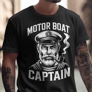 May include: Black t-shirt with a white graphic of a sea captain wearing a hat and smoking a pipe. The text "MOTOR BOAT CAPTAIN" is above and below the illustration. The shirt is a crew neck.