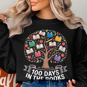May include: Black sweatshirt featuring a colorful tree design with open books, apples, and pencils. The tree is the focal point, with the text "100 DAYS IN THE BOOKS" displayed on a banner below the tree. A fall-themed design.