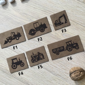 Könnte beinhalten: Sechs braune, rechteckige Aufnäher mit schwarzen Illustrationen von Baumaschinen. Die Aufnäher zeigen einen Frontlader, eine Straßenwalze, einen Bagger, einen Traktor, einen Oldtimer-Traktor und einen Traktor mit Anhänger.