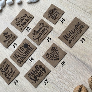 Könnte beinhalten: Zehn braune Leder-Patches mit schwarzem Text. Die Patches zeigen verschiedene saisonale Grüße, darunter "Beach Vibes", "Vacation Mode", "Hello Sunshine", "Hello Summer", "Sunshine Mind", "Welcome Autumn", "Sun and Sand", "Hello Spring" und ein Herz mit Blättern.