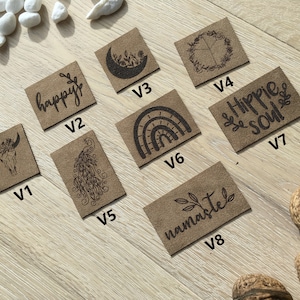 May include: Eight brown leather patches with various designs and text, including "happy", "hippie soul", "namaste", and a rainbow. The patches are arranged in a grid on a wooden surface.