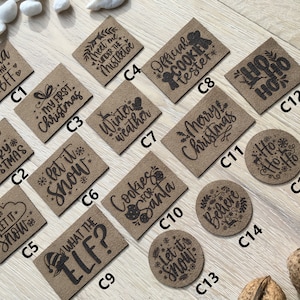 Könnte beinhalten: Eine Sammlung von 15 braunen Papier-Geschenk-Etiketten mit verschiedenen weihnachtlichen Sprüchen. Die Etiketten sind mit schwarzer Tinte verziert und zeigen Sätze wie "Let it Snow", "Merry Christmas", "What the Elf?", "Cookies for Santa" und "Ho Ho Ho".