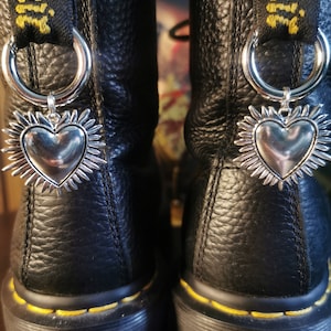 May include: Black leather boots with yellow stitching and a silver heart charm with a sunburst design. The boots have a thick platform sole and a black lace-up closure.