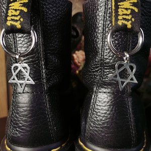 May include: A pair of black leather boots with yellow stitching and a black and yellow strap with the text "Dr. Martens" on each boot. Each boot has a silver charm attached to the strap with a heart and star design.