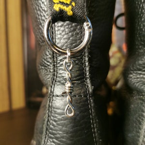 Puede incluir: Botas de cuero negro con una etiqueta amarilla y negra que dice "Dr. Martens" y un llavero plateado con un diseño de alambre de púas.