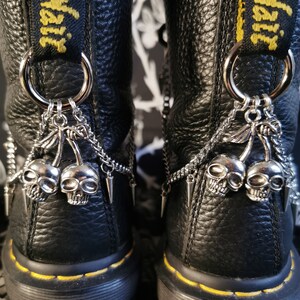 May include: Black leather boots with yellow stitching and silver skull and cherry charms hanging from chains attached to the back of the boots.