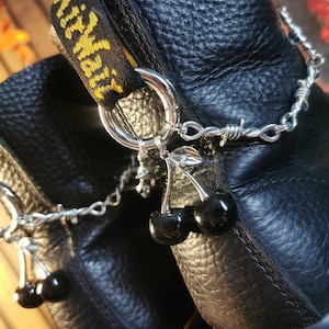 May include: Black leather boots with a yellow and black strap and a silver chain with barbed wire and black cherry charms.