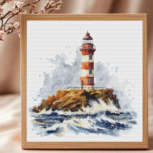 May include: Cross-stitch art of a lighthouse on a rocky island, framed in wood. The lighthouse has red and white stripes, with a dark red top. The sea is depicted with blue and white waves. The artwork is signed "Virola Cross Stitch".