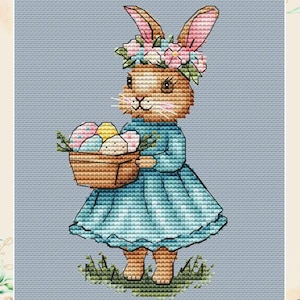 May include: A cross stitch pattern featuring a cute bunny wearing a flower crown and holding a basket of colorful Easter eggs. The bunny is standing on a green patch of grass.