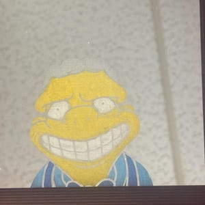May include: Framed cartoon artwork featuring a yellow character with a large grin and white teeth. The character has white hair and is wearing a blue and white striped shirt. The artwork is set against a speckled background.