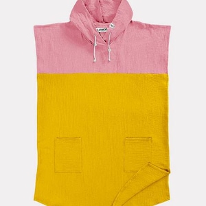 Puede incluir: Un poncho para bebé de dos tonos en rosa y amarillo. La mitad superior es rosa con una capucha con pequeñas orejas de oso. La mitad inferior es amarilla con dos bolsillos cuadrados. El poncho tiene un cordón y está hecho de una tela texturizada.