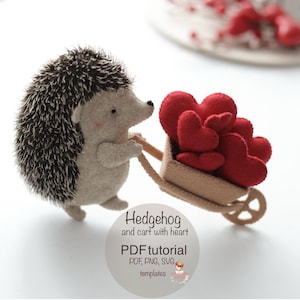 Könnte beinhalten: Eine Filz-Igel-Figur mit hellbraunem Körper und dunkelbraunen Stacheln, die einen kleinen Wagen voller roter Filzherzen zieht. Der Wagen ist hellbraun. Der Text "Hedgehog and cart with heart" und "PDF tutorial" ist enthalten.