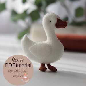 Pode incluir: Um ganso de feltro branco feito à mão com bico e pés castanhos. O ganso tem detalhes costurados e um corpo arredondado. O texto na imagem diz "Goose PDF tutorial" com opções de tipo de arquivo. É um projeto de artesanato.