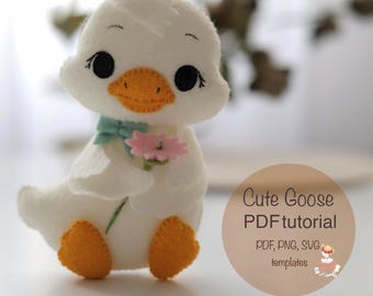 Puede incluir: Una muñeca de ganso de fieltro blanco hecha a mano con ojos negros, pico naranja y patas naranjas. El ganso sostiene una flor rosa y lleva un lazo azul claro. La imagen incluye el texto "Cute Goose PDF tutorial".