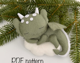 May include: A green felt dragon with white eyes and a white horn sleeping on a white cloud. The dragon has a stitched-on smile and closed eyes. The image includes the text "PDF pattern".