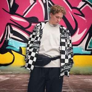 May include: A person wearing a black and white checkered jacket with the word "Stain" printed on it, a white t-shirt, black pants, and a black fanny pack. The background features colorful graffiti art.