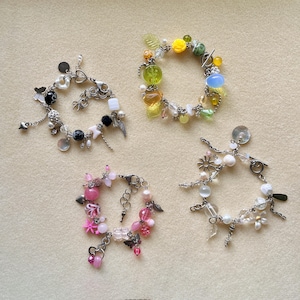 May include: Four beaded bracelets with various charms and beads. One bracelet features black and white beads with silver charms. Another has yellow, green, and blue beads. A third bracelet has pink beads and charms, and the last has white and clear beads.