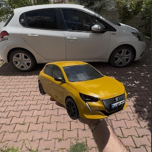 May include: A yellow toy car with black wheels is held in front of a white car. The toy car has a detailed design, including headlights and a grille. The background features a brick patio and greenery.