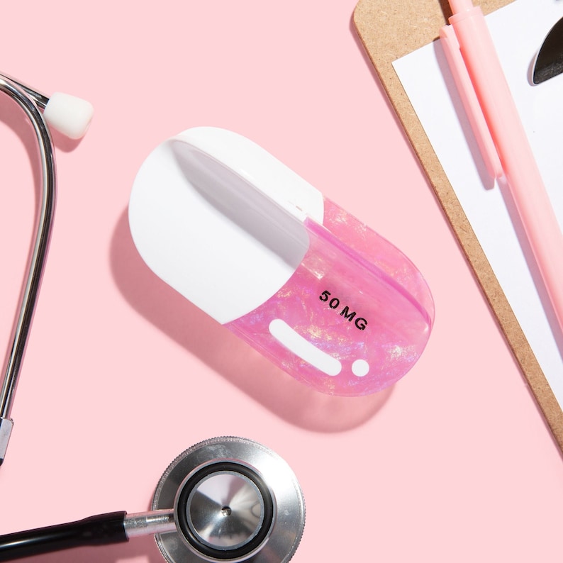 Op de afbeelding: Een roze pilvormige container met een wit deksel en de tekst "50 MG" erop gedrukt. De container staat op een roze oppervlak naast een stethoscoop.