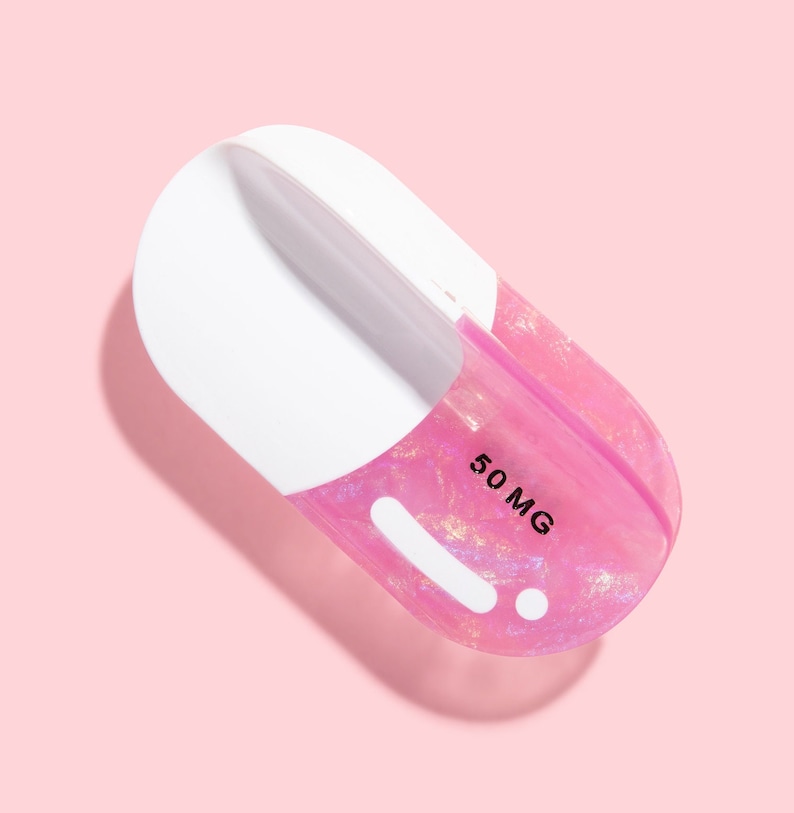 Op de afbeelding: Een roze en witte pilvormige container met een glinsterende afwerking. De container heeft een wit label met de tekst "50 MG" erop gedrukt.