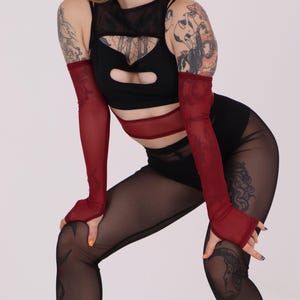 May include: A woman wearing a black mesh top with a red mesh band around the waist and red mesh fingerless gloves. She is also wearing black mesh leggings with a tattoo on her leg.