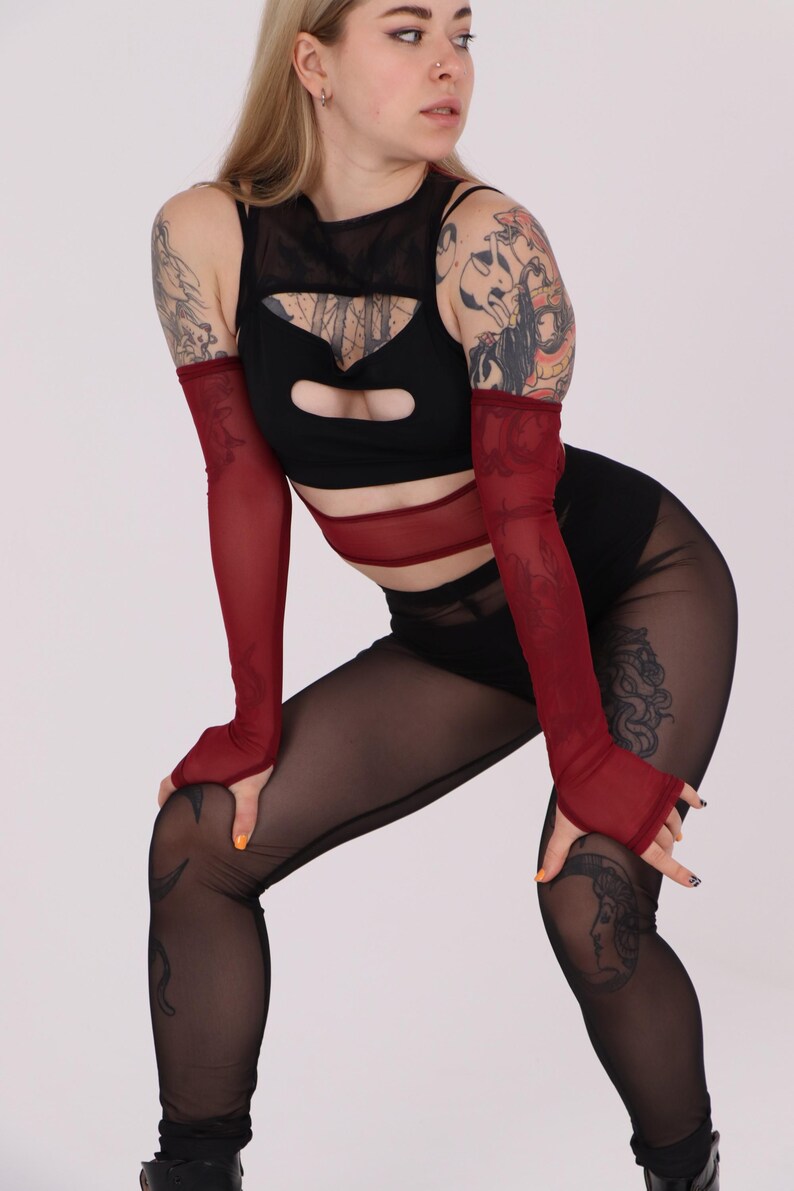 May include: A woman wearing a black mesh top with a red mesh band around the waist and red mesh fingerless gloves. She is also wearing black mesh leggings with a tattoo on her leg.