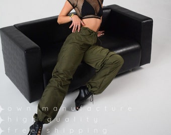 May include: A woman wearing a black mesh top, black bra, olive green cargo pants, and black lace-up heels sits on a black leather couch.