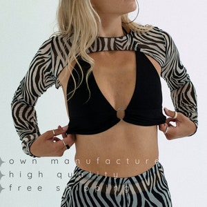May include: A black mesh crop top with a zebra print overlay. The top has a cut-out design and a ring detail at the center. The model is wearing a matching zebra print skirt.