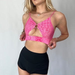 May include: A pink snakeskin print crop top with a cut-out detail and a ring accent. The top is paired with black high-waisted shorts.