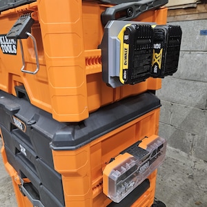 May include: An orange and black rolling tool chest with the Klein Tools logo. The chest has multiple compartments and drawers. Two black and yellow DeWalt 20V batteries are attached to the side. A clear plastic storage container is also attached.