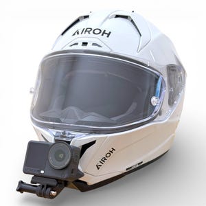 Könnte beinhalten: Weißer Motorradhelm mit klarem Visier und einer schwarzen Action-Kamera. Der Helm trägt den Markennamen "AIROH" in Schwarz. Die Kamera ist am Kinn des Helms befestigt.