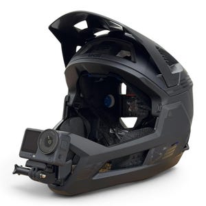 May include: A matte black full-face mountain bike helmet featuring a prominent visor, ventilation ports, and internal padding. A small action camera is securely mounted to the front chin bar of the helmet, positioned to capture forward-facing footage.
