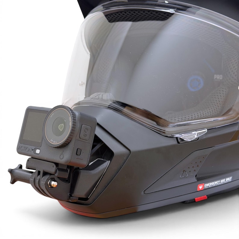 Puede incluir: Casco de moto negro con visera transparente y c&aacute;mara de acci&oacute;n adjunta. La c&aacute;mara est&aacute; montada en la parte delantera del casco y es negra con una lente y una peque&ntilde;a pantalla. El casco tiene la palabra "PRO" impresa en el lateral.