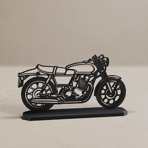 May include: A black metal silhouette of a motorcycle mounted on a rectangular base. The design features a detailed outline of the frame, engine, wheels with spokes, seat, handlebars, and exhaust pipe, presented as a flat, two-dimensional object.