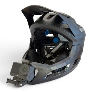 以下が含まれることがあります： 黒とグレーのマウンテンバイク用ヘルメット。アクションカメラが取り付けられています。ヘルメットにはバイザーと内側のパッドが付いています。カメラは黒色でレンズが付いています。ヘルメットには「Leatt」と「Enduro」の文字がプリントされています。
