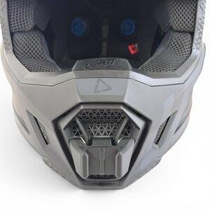 May include: A close-up view of a gray motocross helmet. The helmet features a geometric design on the chin guard and the brand name "LEATT" is visible. The interior padding is gray and the helmet has blue accents.
