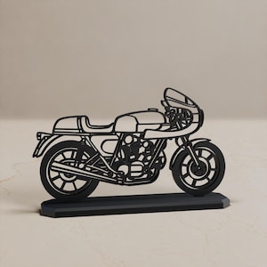 May include: A black, flat, laser-cut metal silhouette of a cafe racer motorcycle. The design features a detailed frame, engine, spoked wheels, and a front fairing, all mounted on a rectangular black base for stability and display purposes.