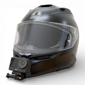Puede incluir: Casco de moto negro mate con visera transparente y cámara de acción montada. El casco tiene el logo "agu". La cámara de acción negra está montada debajo de la visera y tiene la palabra "ACTION".