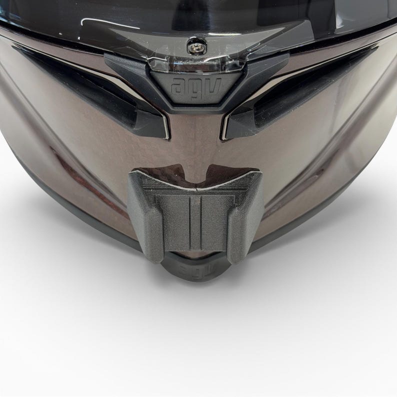 Pu&ograve; includere: Primo piano di un casco da moto con finitura marrone metallizzato lucido. Il casco presenta una visiera nera e uno spoiler per il mento nero. Il marchio "AGV" &egrave; visibile sulla parte anteriore.