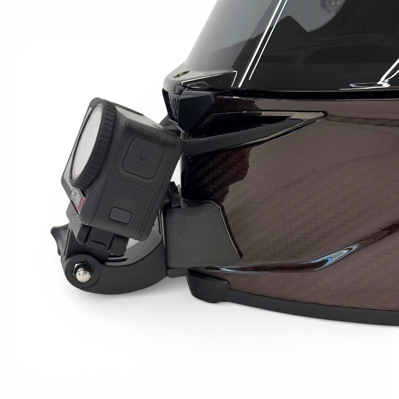 Pu&ograve; includere: Una action camera nera montata su un casco da moto nero. La fotocamera &egrave; quadrata con un obiettivo e pulsanti laterali. Il casco ha una finitura lucida e un motivo in fibra di carbonio.