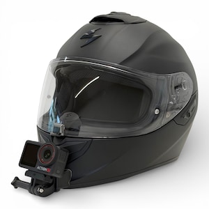 Puede incluir: Casco de moto negro mate con visera transparente y cámara de acción montada. El casco presenta un logotipo de Scorpion y un diseño aerodinámico. La cámara de acción es negra y roja, con el texto "ACTION S1" visible.